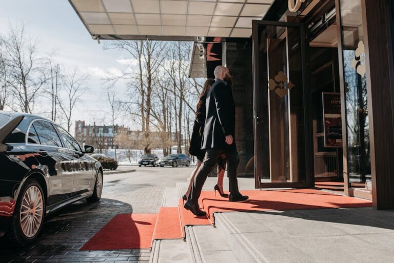 A man and woman elegantly dressed enter a luxury hotel, walking on a red carpet.