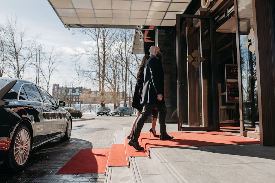 A man and woman elegantly dressed enter a luxury hotel, walking on a red carpet.