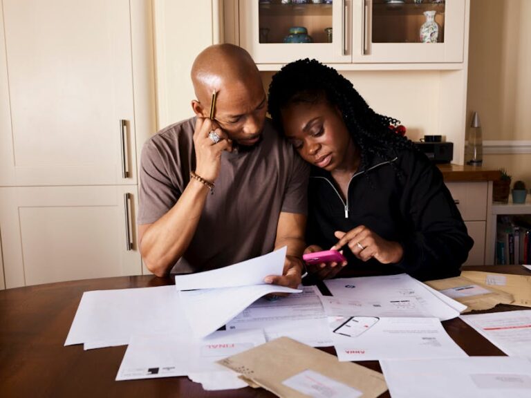 A couple sits at a table managing domestic finances, evaluating documents and using a smartphone.