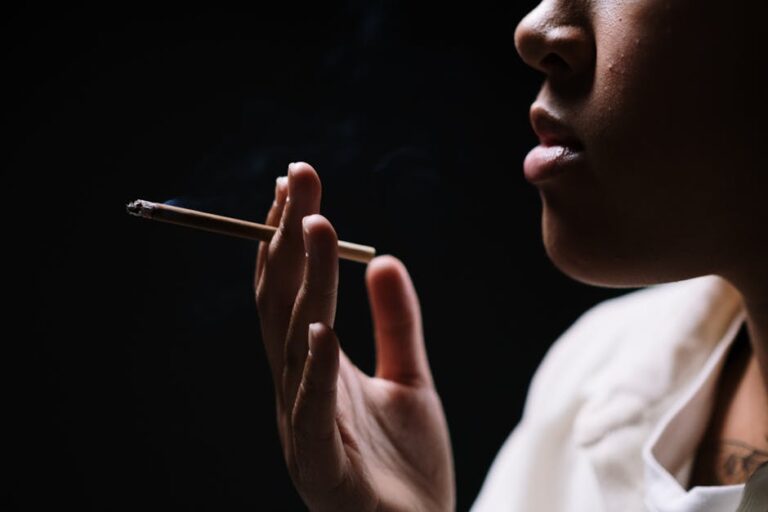 A close-up of a person holding and smoking a cigarette against a dark background.